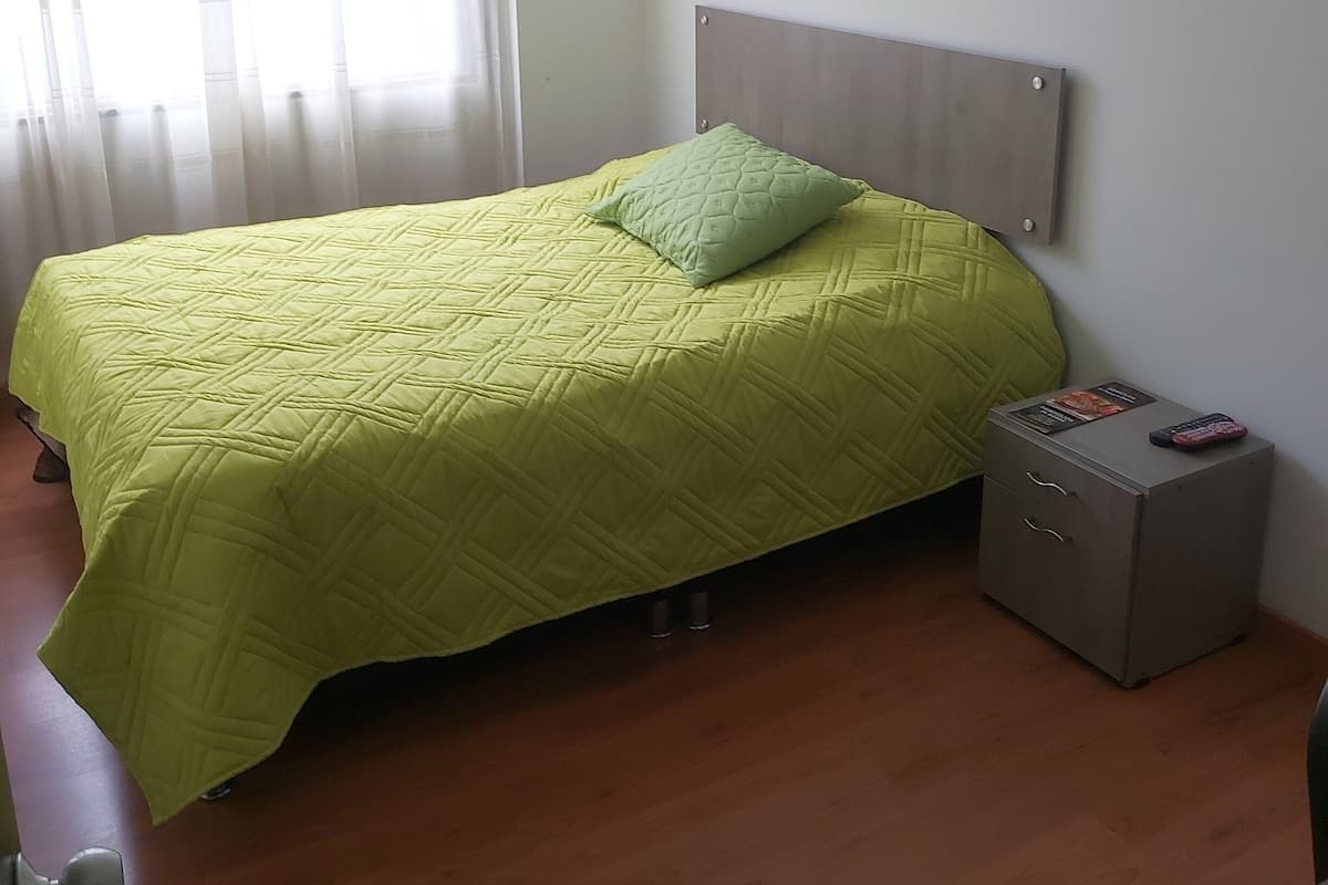 A bedroom with a bed, a nightstand, and a window with curtains.