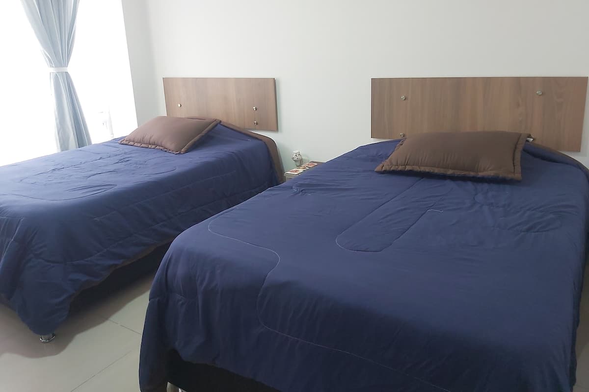 Two twin beds with wooden headboards, blue bedding, and brown pillows in a room with white walls and a tiled floor.