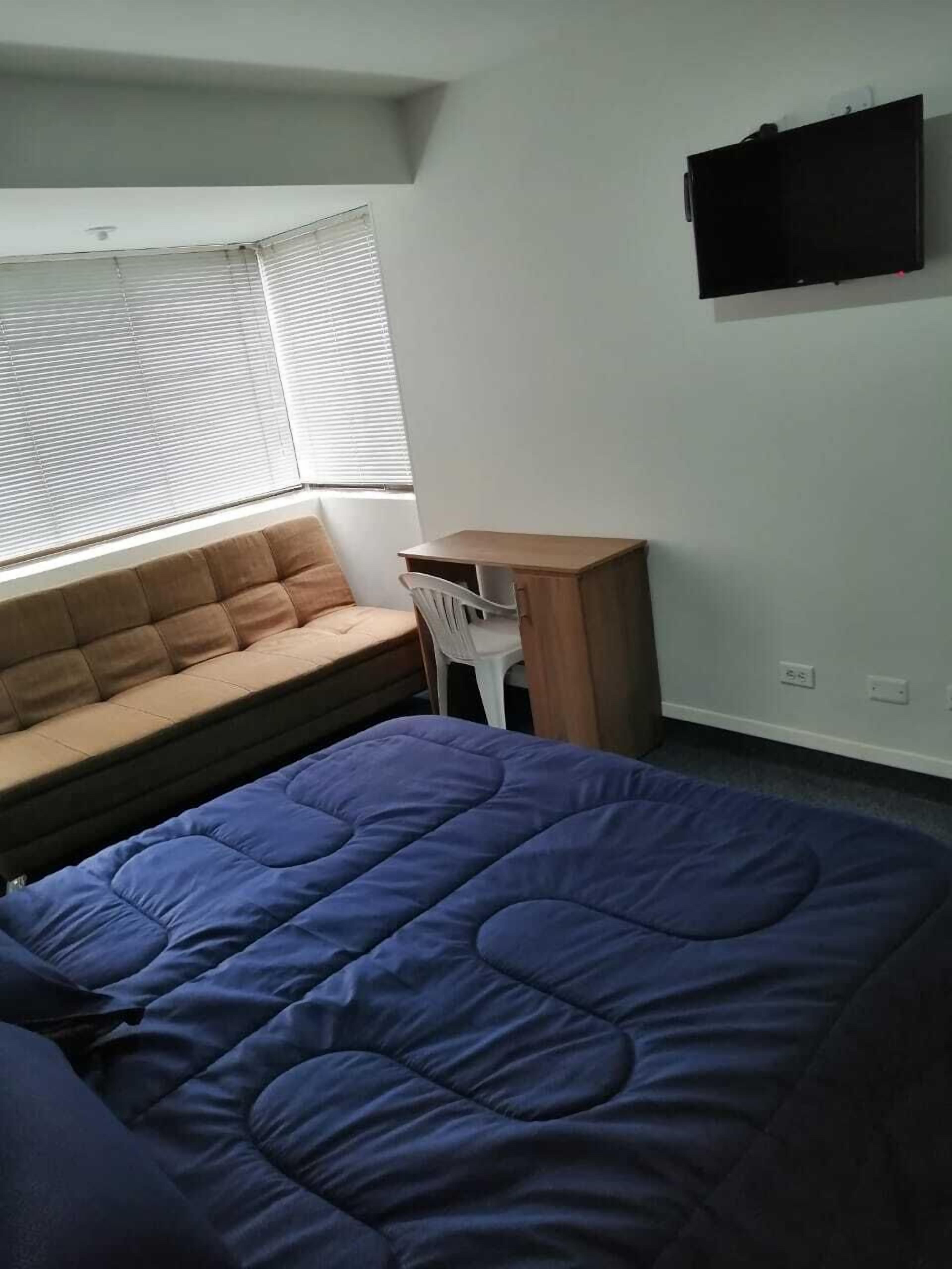 A bedroom with a bed, a window with blinds, a small desk, and a chair.