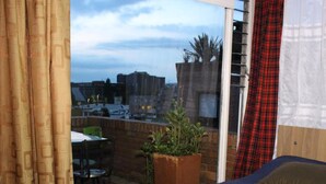 Un dormitorio con una cama, una planta en maceta y vista a la ciudad a través de una ventana.