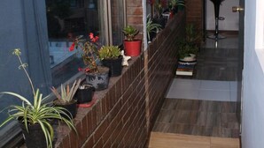 Un pasillo estrecho con suelo de madera, pared de ladrillo y una ventana con plantas en macetas.