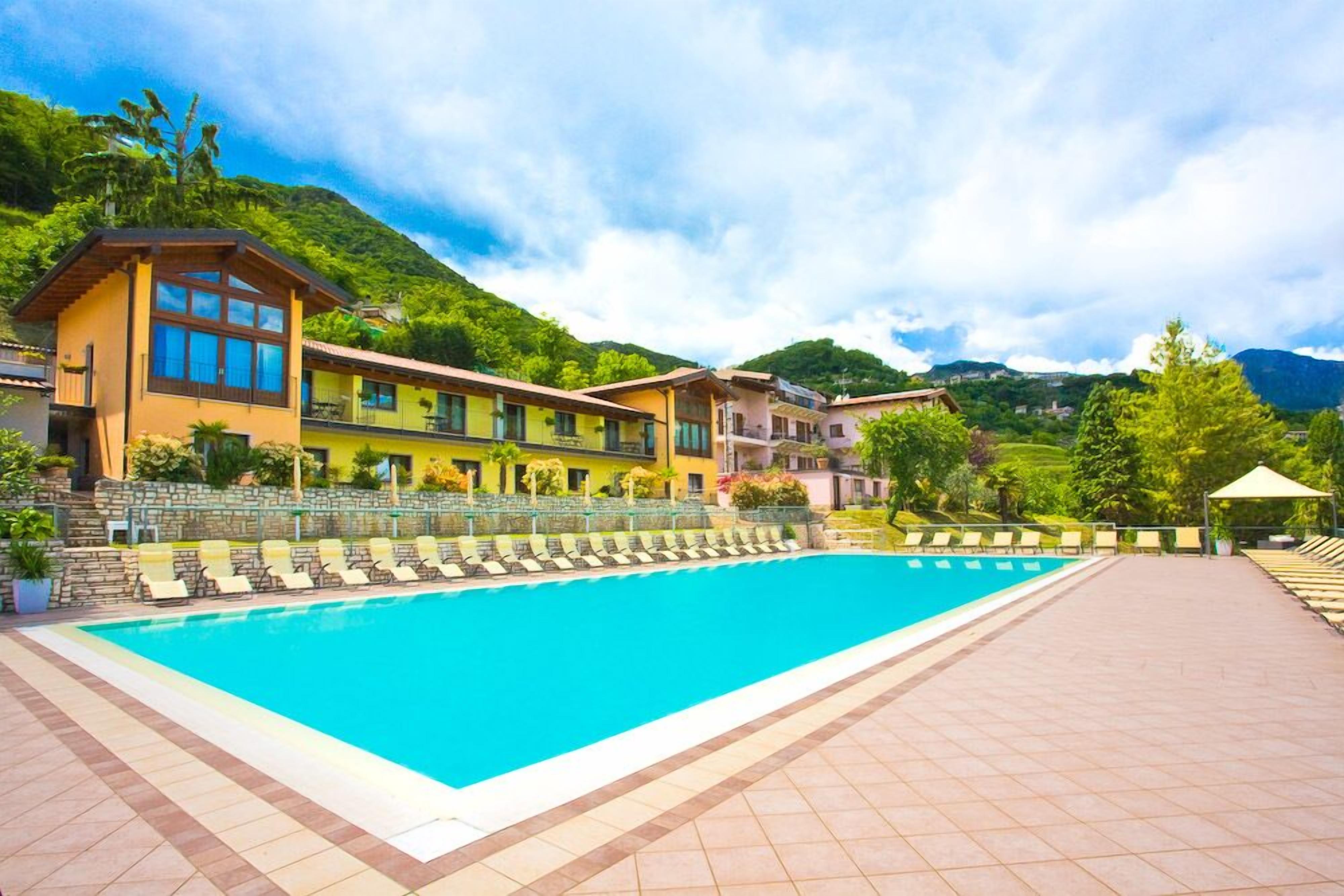 A swimming pool with lounge chairs, a stone wall, and buildings with balconies.