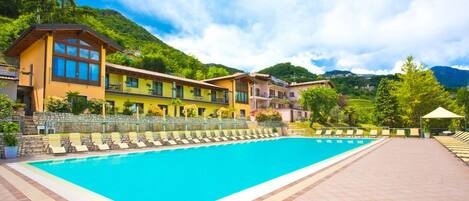 A swimming pool with lounge chairs, a stone wall, and buildings with balconies.