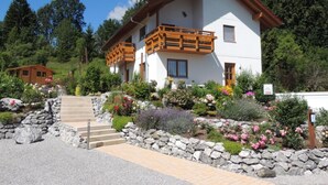A two-story chalet with a wooden balcony, surrounded by a well-maintained garden with various plants and flowers. - Appartement am Rosengarten (Füssen)