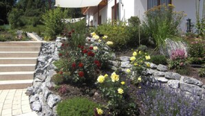 A garden with a variety of flowers and a stone wall. - Appartement am Rosengarten (Füssen)