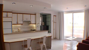A modern kitchen with white cabinets, a central island, and two white chairs. - Pi Sunyer 4 4B - Studio Apartment, Sleeps 2 (Roses)