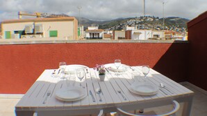 A table set for two with white plates, cutlery, and glasses, overlooking a town with buildings and a hill in the background. - Pi Sunyer 4 4B - Studio Apartment, Sleeps 2 (Roses)