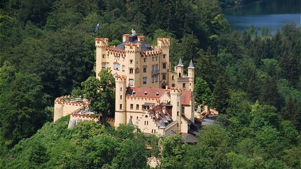 Un château entouré d’une forêt dense et bordé d’un lac.