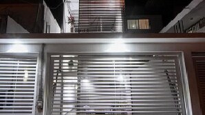 Une porte de garage en métal fermée, composée de lames horizontales, un sol en béton et, au fond, un bâtiment doté d’un toit en pente.