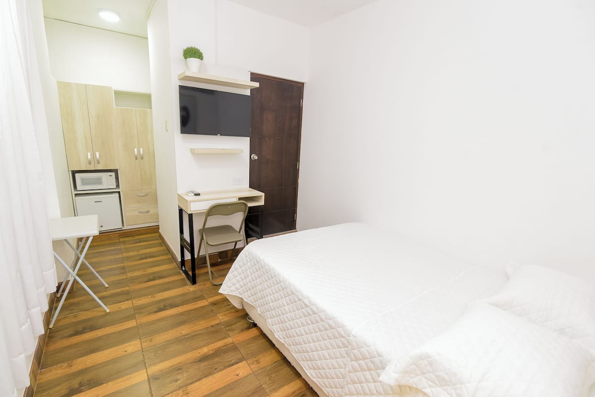 Quarto com cama, escrivaninha, cadeira, guarda-roupa e micro-ondas.