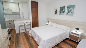 Une chambre comprenant un lit, une table de chevet, une chaise, un bureau et un coin cuisine.