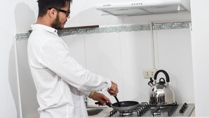 Une personne cuisine dans une cuisine équipée d’une cuisinière à gaz et d’une bouilloire.