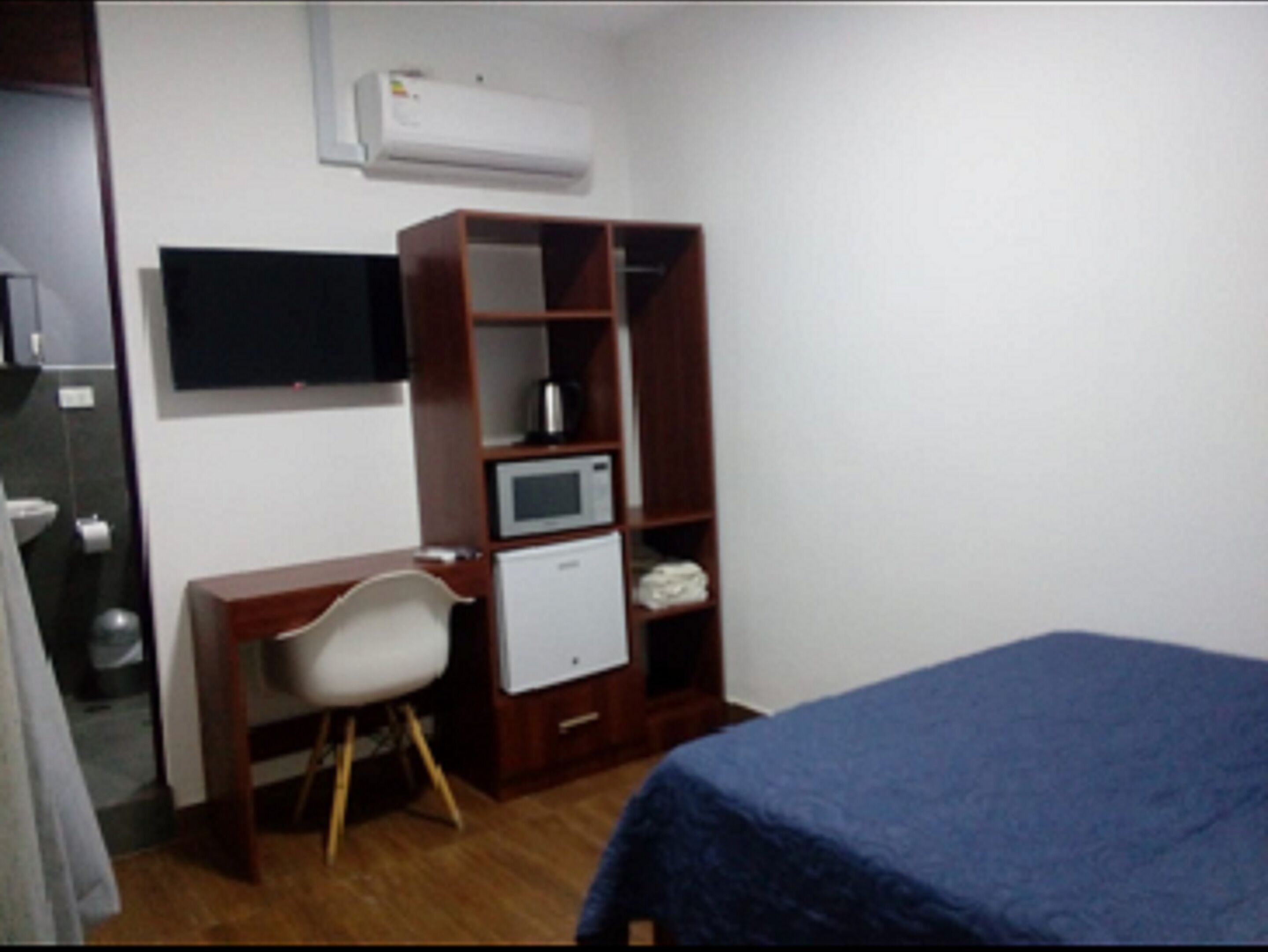 Un dormitorio pequeño con cama, escritorio, silla, armario, televisor y microondas.