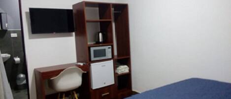 Un dormitorio pequeño con cama, escritorio, silla, armario, televisor y microondas.