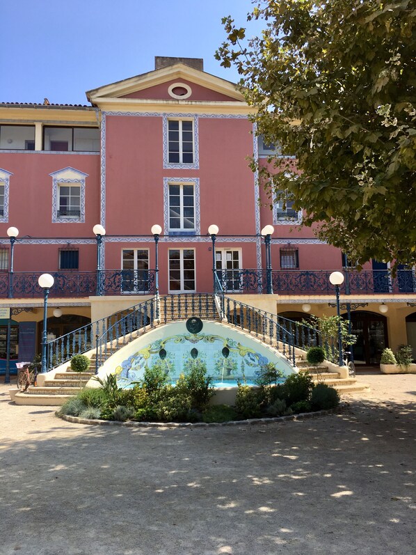 Un edificio con una escalera central, varias ventanas y una fuente decorativa en la fachada.