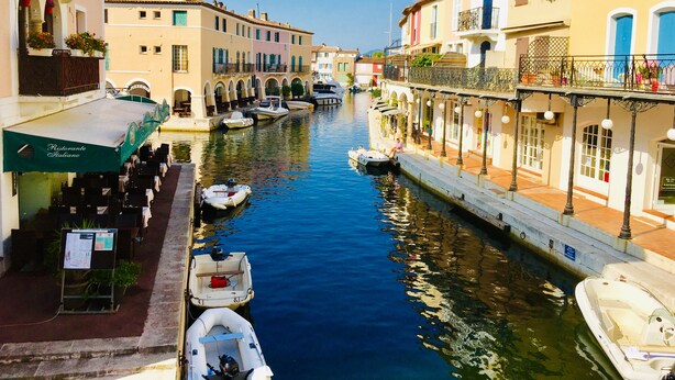 Un canal estrecho bordeado por edificios con terrazas al aire libre y barcos amarrados a lo largo de las orillas.