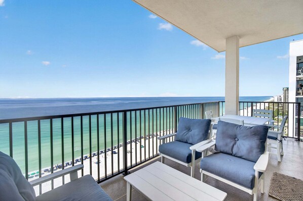 A balcony with a view of the ocean, white furniture, and a clear sky.