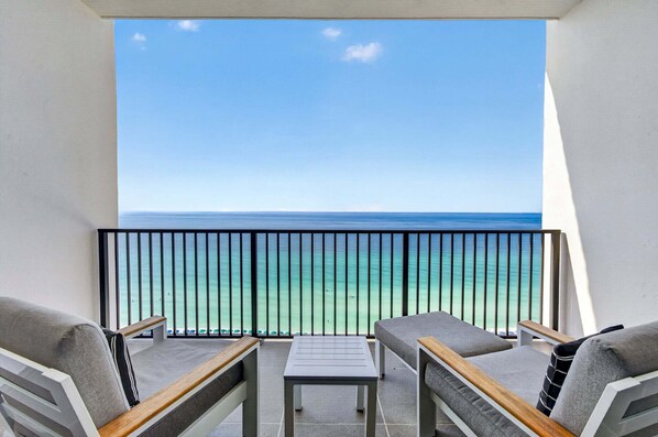 A balcony with a view of the ocean, equipped with two chairs and a small table.