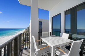 A balcony with a white table and chairs overlooking a beach.