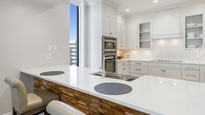 Una cocina moderna con armarios blancos, horno integrado, pileta y comedor con dos sillas.