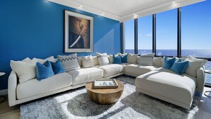 Una sala de estar moderna con un amplio sofá modular, una mesa redonda y un gran ventanal con vistas al océano.