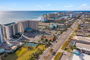 An aerial view of a coastal city with a prominent hotel complex, wide roads, and a beach in the background.