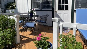 Um pátio com mesa e cadeiras, um guarda-sol azul e plantas em vasos.