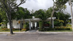A building with a covered entrance, surrounded by greenery and palm trees. - Violet House - Riviera Maya (Puerto Morelos)