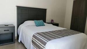 A neatly made bed with a striped blanket, a teal pillow, and a small bedside table with a vase of flowers. - Violet House - Riviera Maya (Puerto Morelos)