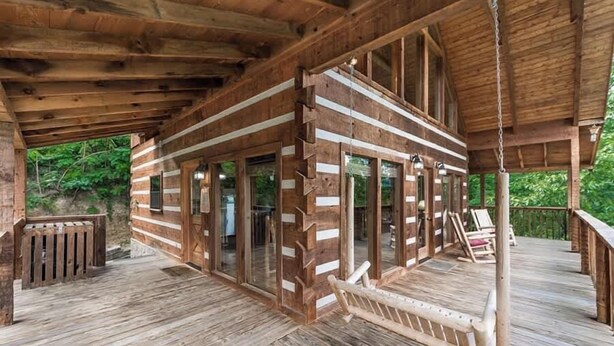 Una cabaña de madera con terraza, ventanas amplias y un columpio colgante.