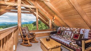 Un interior de madera acogedor con un sofá, una mecedora, una mesa de madera y un ventanal con vistas a un paisaje montañoso.