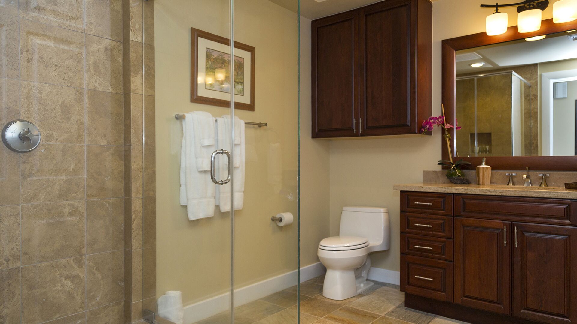 A bathroom with a glass shower enclosure, a toilet, and wooden cabinets.