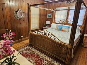 Een hemelbed met hemeltje, houten wanden, een decoratieve spiegel en een bloemstuk.