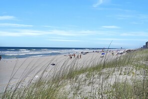 En strand med mennesker, klitter og en klar himmel.