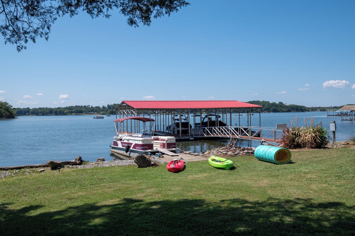 A lakeside dock with a covered seating area, a boat, and floating docks.
