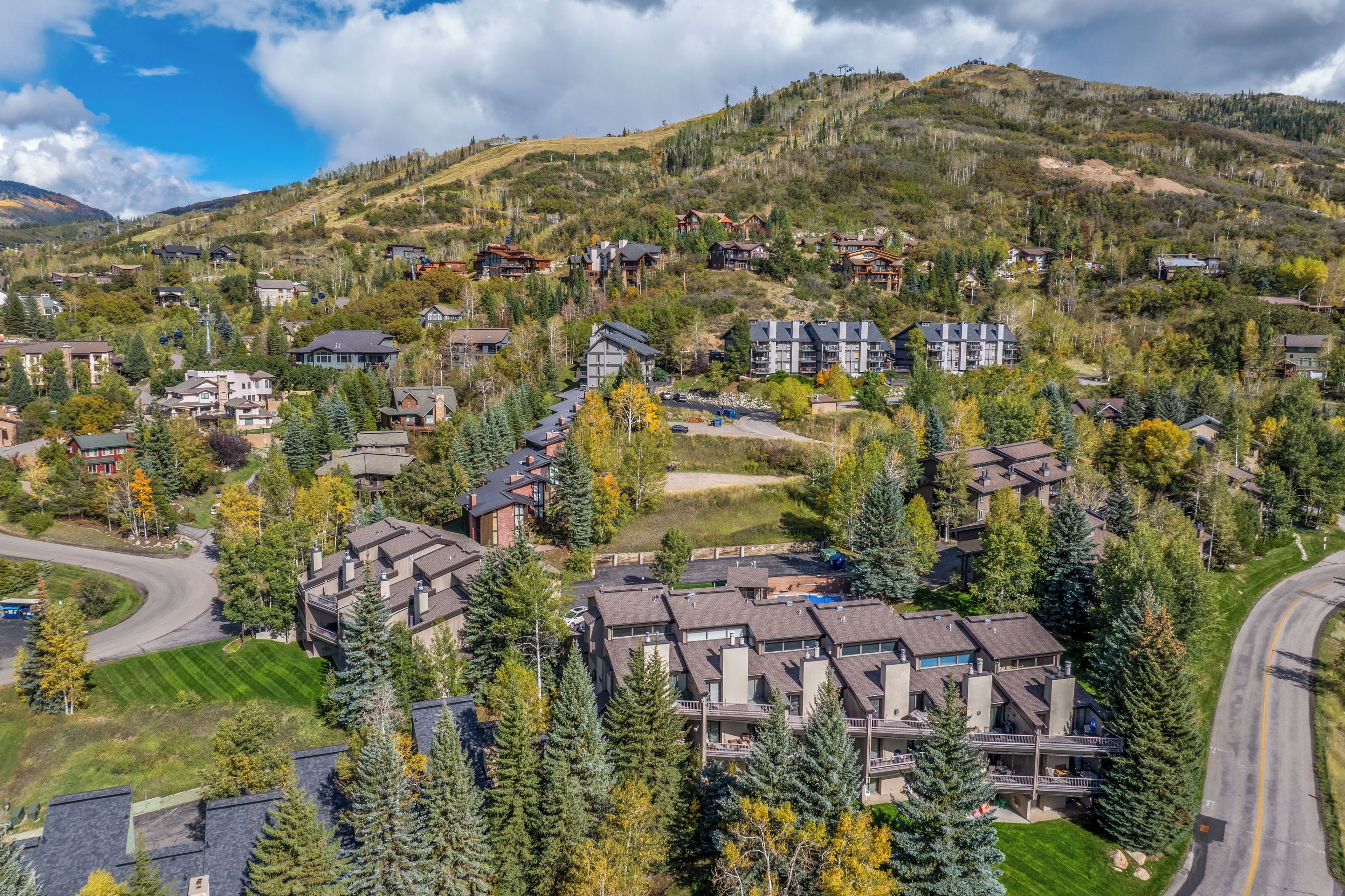 A residential area with multiple two-story houses, a winding road, and a mountainous backdrop.