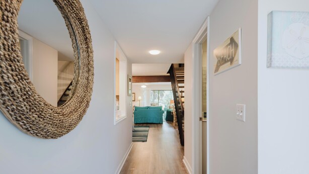 Un couloir avec un miroir à motifs tissés, un canapé de couleur turquoise et un escalier.