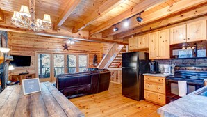 Een chaletinterieur met houten inrichting, een keuken met koelkast, fornuis en magnetron, een eethoek met tafel en stoelen, en een trap naar een terras.