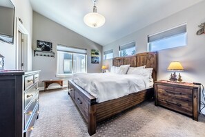 Quarto com cama de madeira, mesas de cabeceira, cômoda e luminária no teto.
