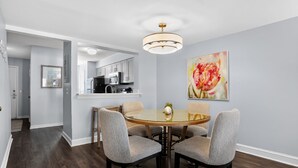Un coin repas avec une table ronde et quatre chaises, une cuisine en arrière-plan et un luminaire au plafond.