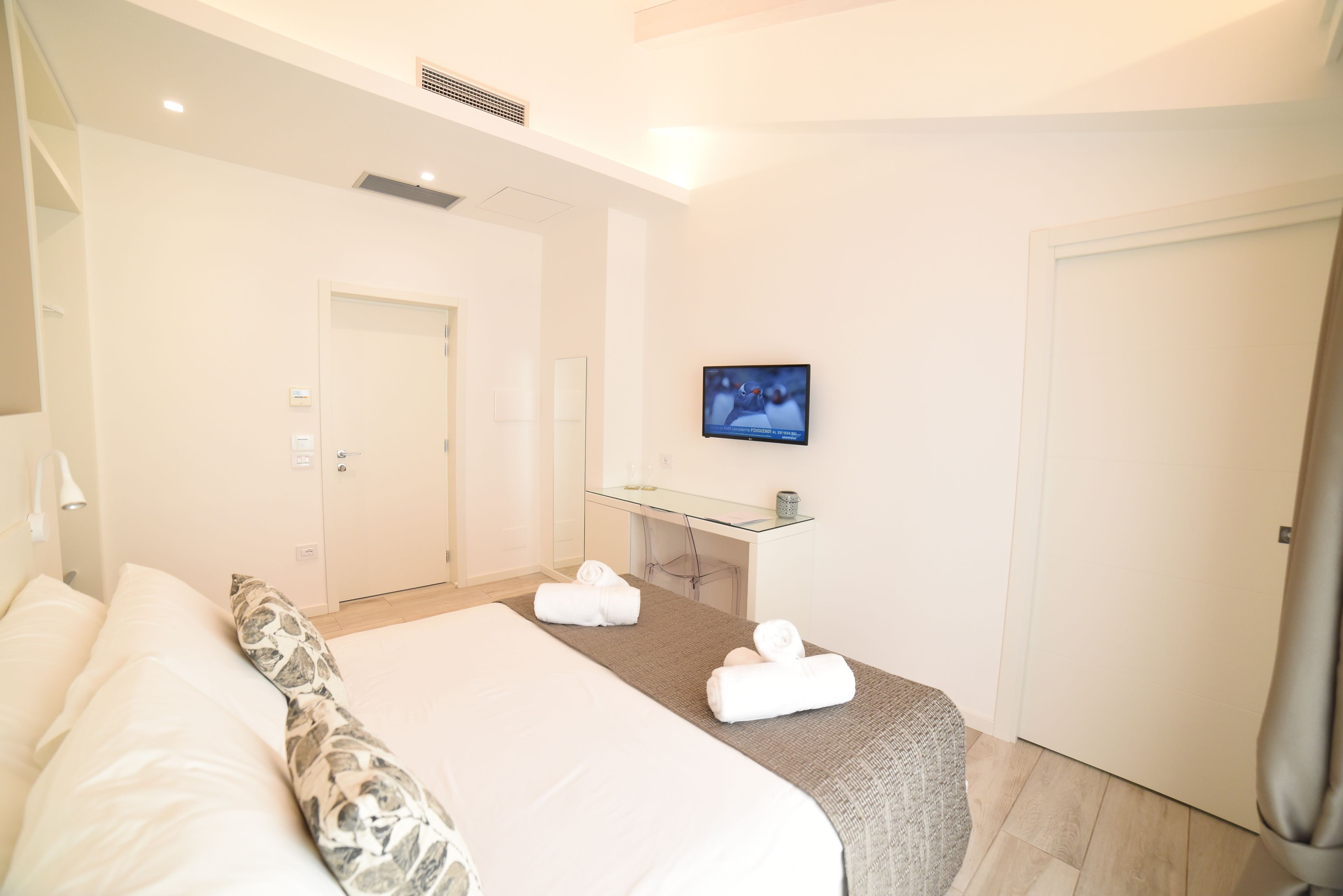 A hotel room with a large bed, a glass desk, a television, and a door.