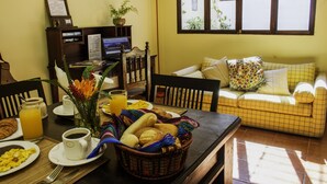 A dining area with breakfast items, a laptop, and a sofa with cushions. - Casita Los Tecolotes (Antigua Guatemala)