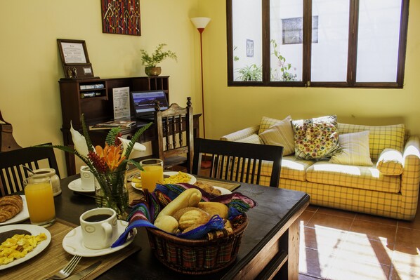 A dining area with breakfast items, a laptop, and a sofa with cushions.