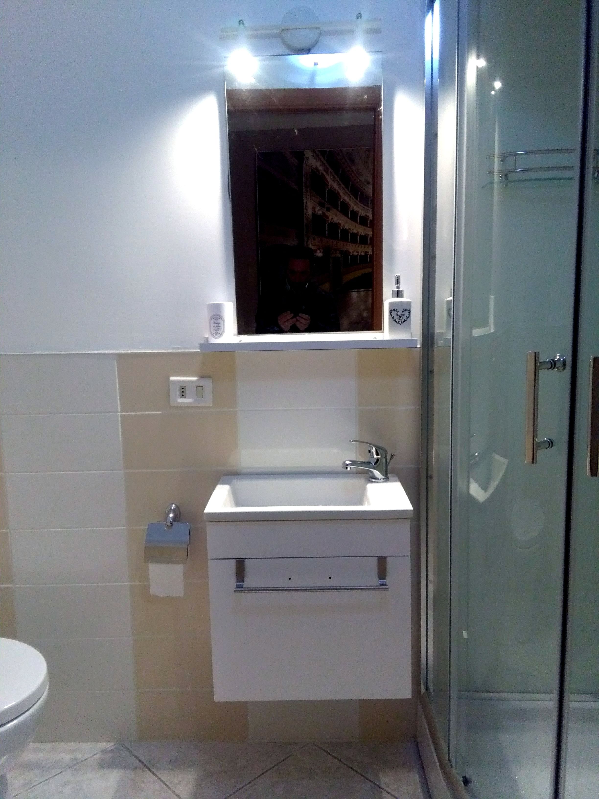 Een badkamer met een witte wastafel, spiegel en toilet. Er is een douchecabine van glas en een handdoekhouder.