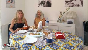 Two people seated at a round table with a floral tablecloth, plates, cups, and a variety of food items. - B&B Salita Metello (Agrigento)