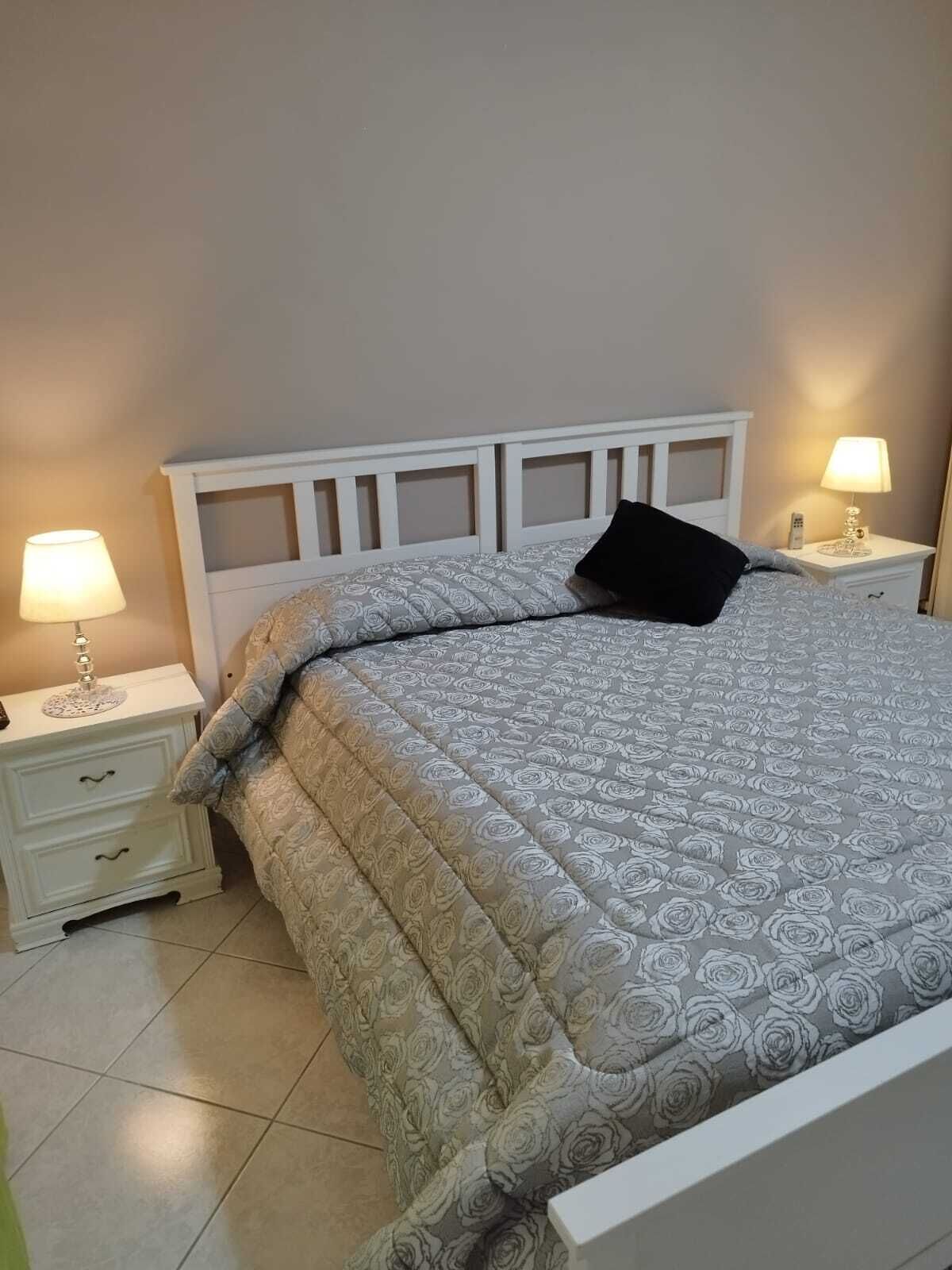 A neatly made bed with a patterned bedspread, two bedside tables with lamps, and a white headboard.