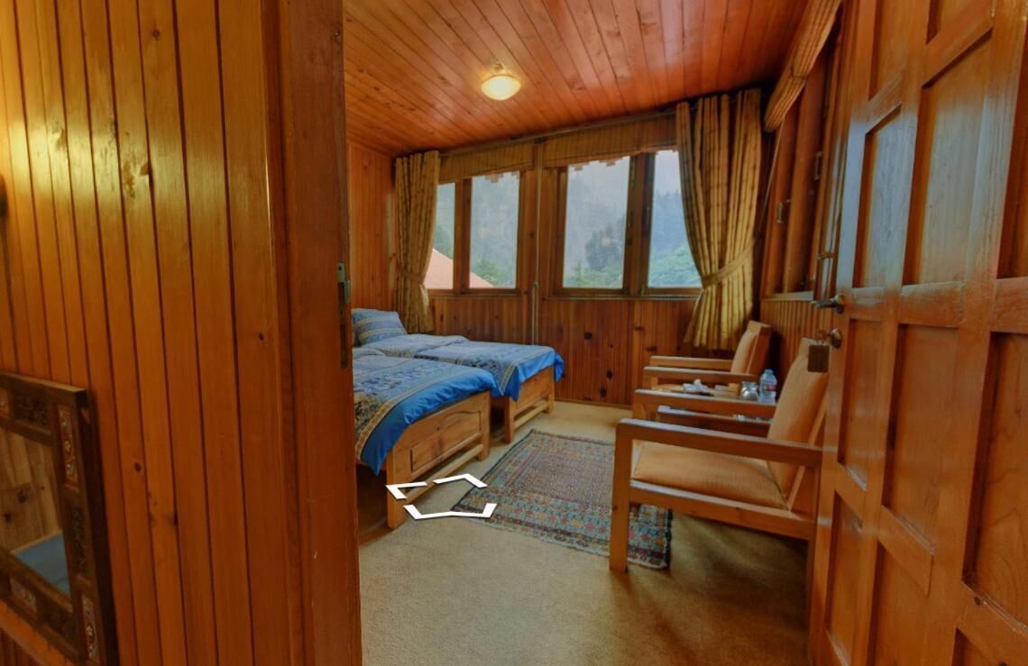 A wooden cabin room with two beds, a desk, and a chair.