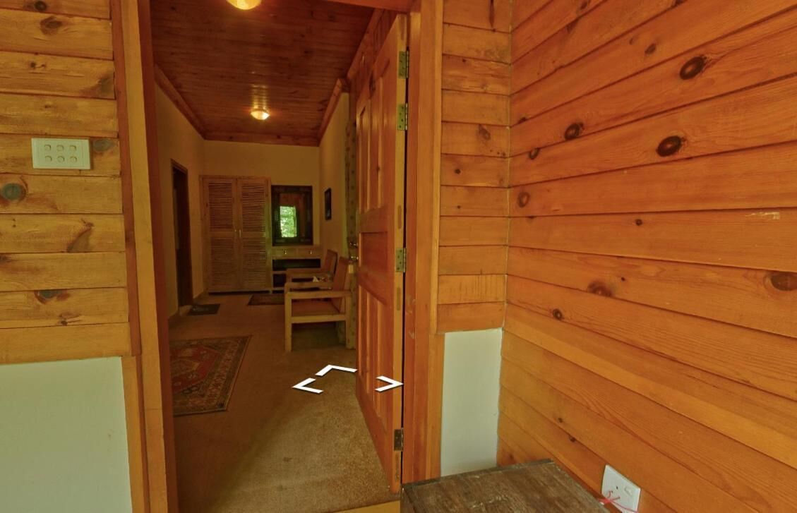 A wooden interior with a hallway leading to a room with a bed and a window.
