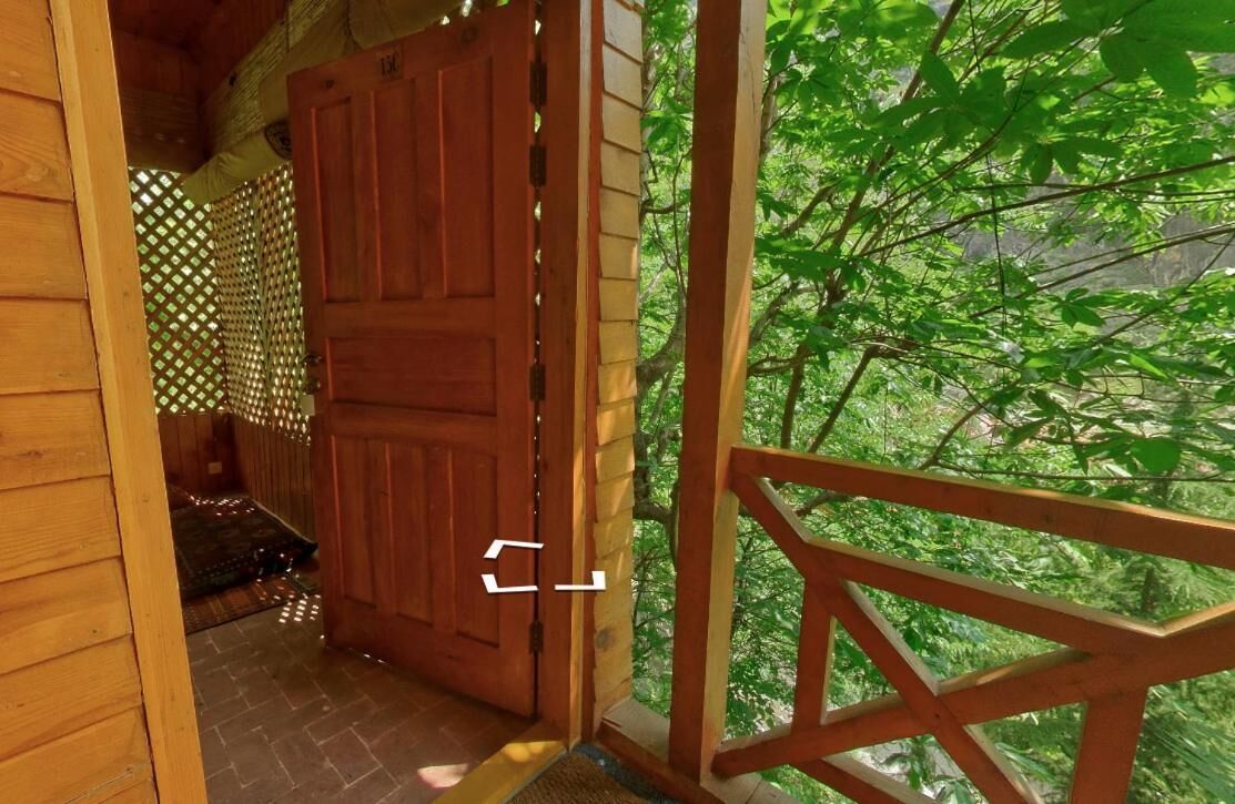 Una puerta de madera que da a un porche cubierto con vistas a un bosque verde y frondoso.