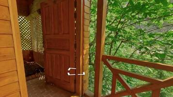Una puerta de madera que da a un porche cubierto con vistas a un bosque verde y frondoso.